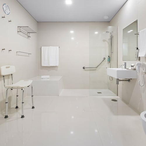Esta é uma casa de banho moderna e acessível, equipada com um duche walk-in, lavatório, sanita, bidé, e várias barras de apoio e uma cadeira de duche.