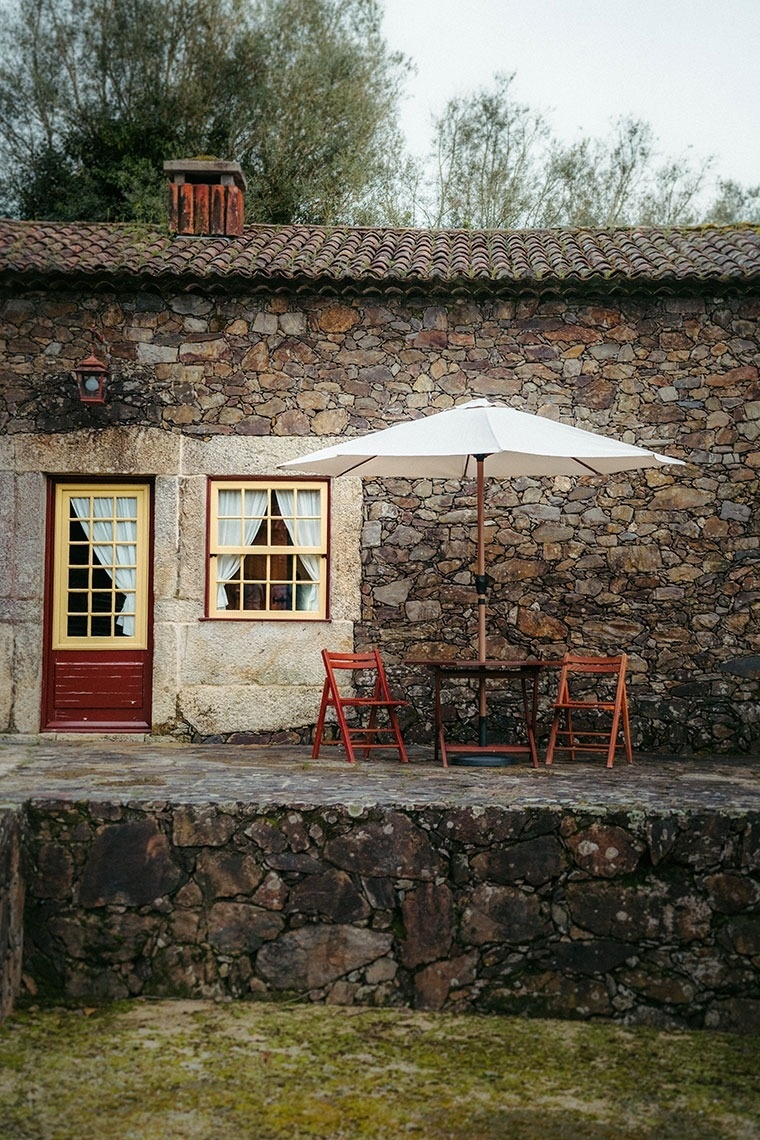 uma mesa com cadeiras e um guarda-chuva em frente a uma casa de pedra