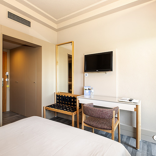 Habitación de hotel con cama, escritorio, silla y TV. Axis: Corporate.