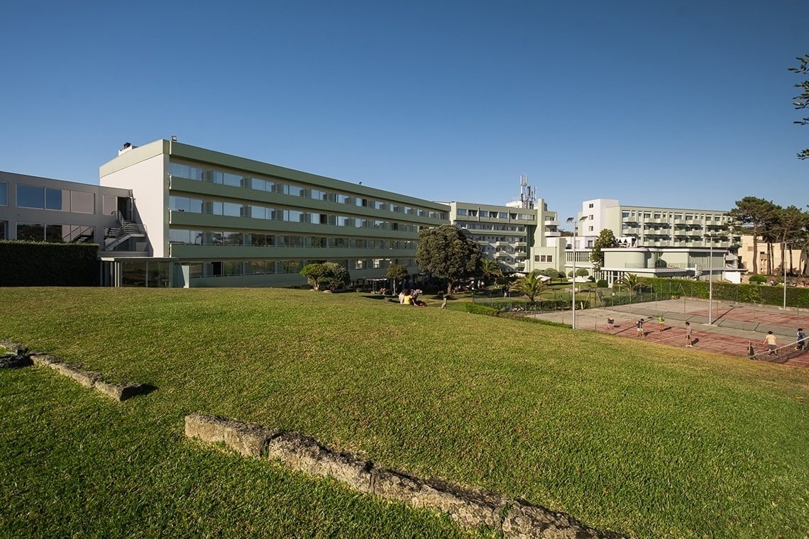 um grande prédio verde e branco com uma quadra de tênis ao fundo