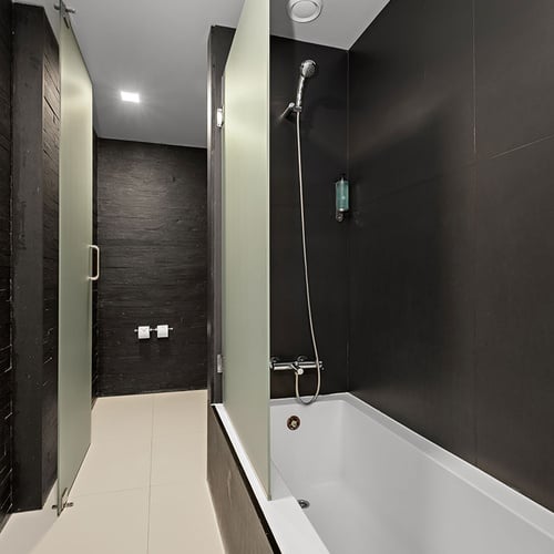 Um banheiro moderno e elegante com paredes escuras, piso claro, uma banheira com chuveiro e divisórias de vidro fosco.