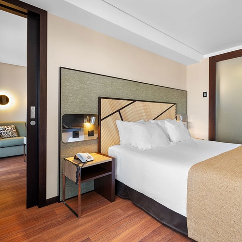 Um quarto de hotel moderno com uma cama e uma área de estar adjacente visível através de uma porta aberta.