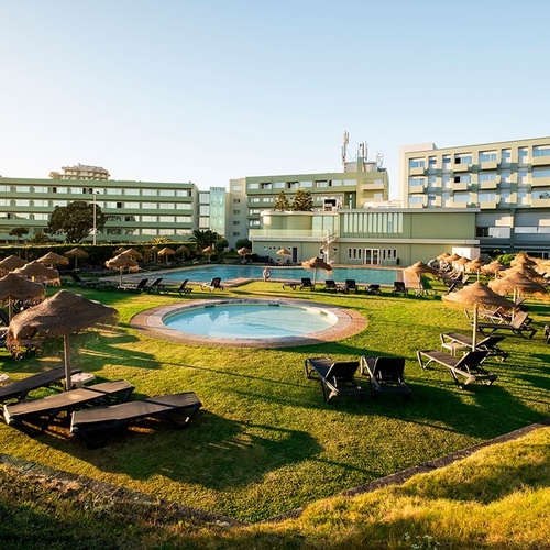 a swimming pool surrounded by chairs and umbrellas with a large building in the background