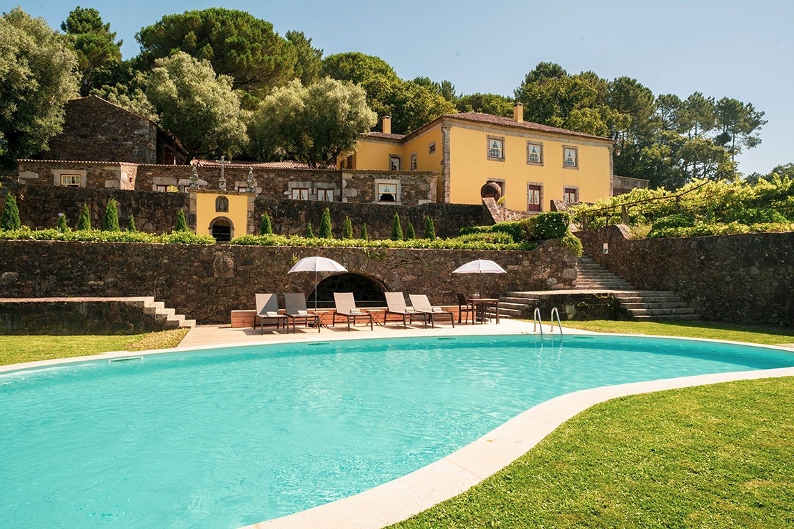 uma grande piscina com cadeiras e guarda-chuvas em frente a uma grande casa