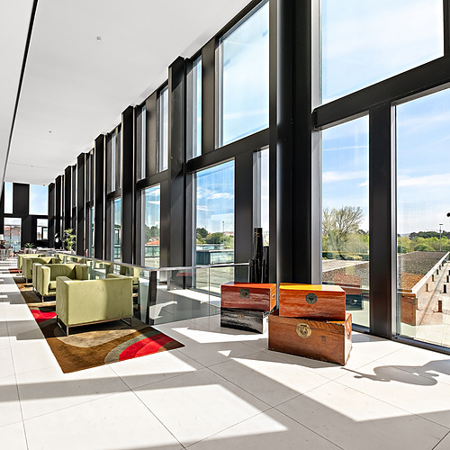 Lounge moderna com poltronas verdes, arte colorida e grandes janelas com vista para o exterior. Axis: Corporate.
