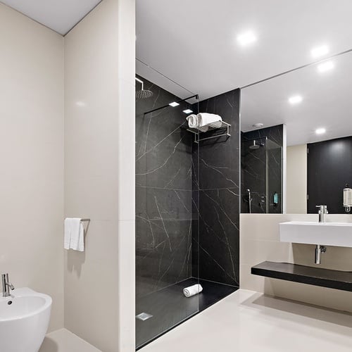 Um banheiro moderno com azulejos claros, uma área de chuveiro em mármore preto, bidê e uma bancada com pia e espelho.