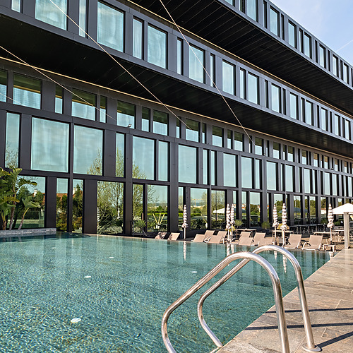 PiscinaAxis: Corporate com escada cromada, espreguiçadeiras e vista para um edifício moderno.