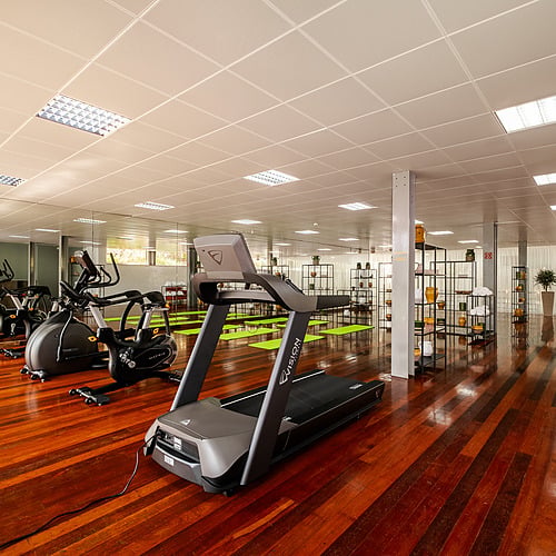 Gimnasio moderno con máquinas de entrenamiento, alfombras verdes y suelos de madera brillante, ideal para tu Axis: Corporate.