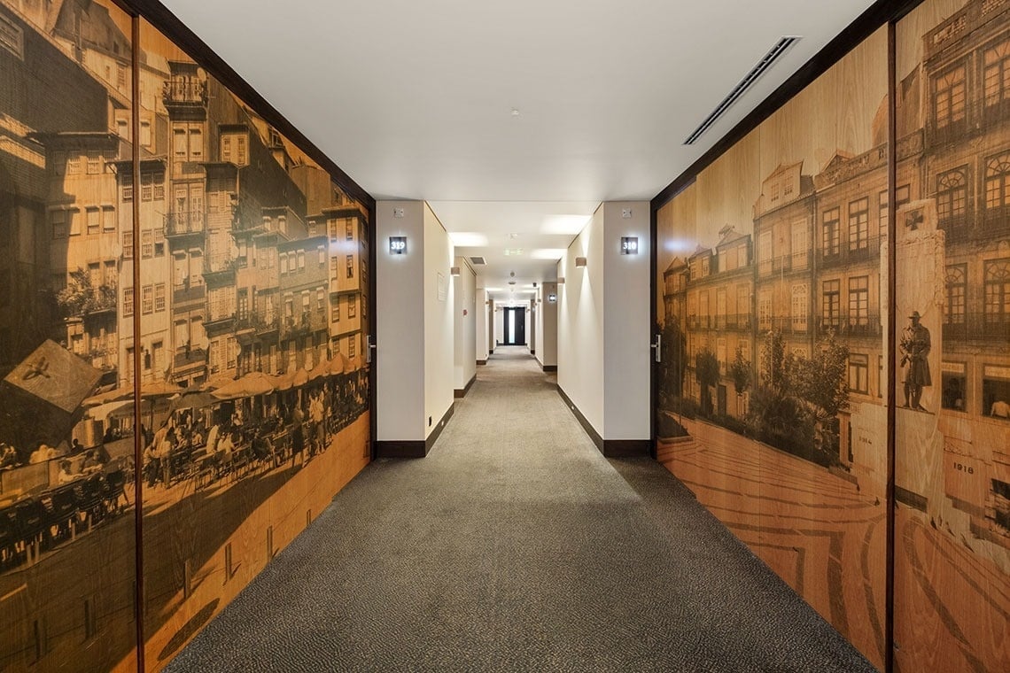 Um corredor de hotel moderno com paredes decoradas com painéis de madeira apresentando imagens em sépia de uma paisagem urbana antiga.