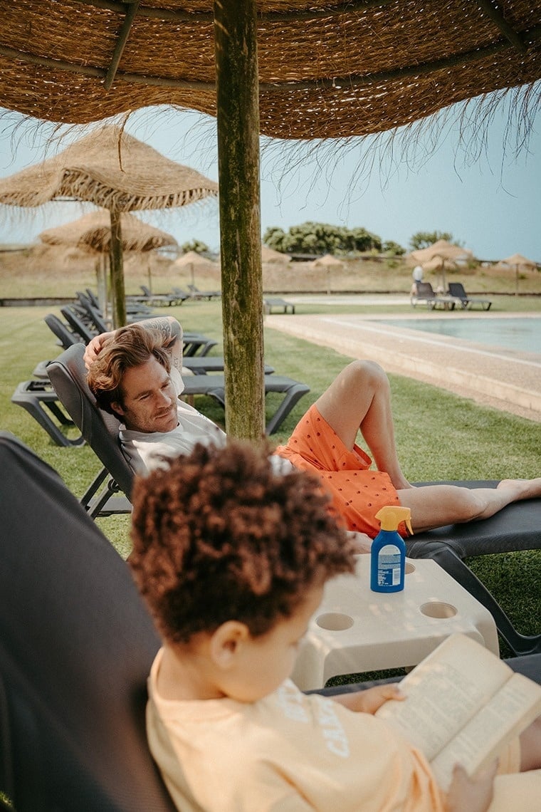 um homem está deitado em uma espreguiçadeira ao lado de um menino que está lendo um livro