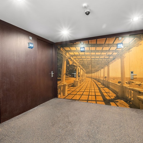 Um corredor com piso acarpetado, portas escuras de madeira e um grande mural fotográfico de uma pérgula costeira que se estende por várias portas com os números de quarto 413, 414 e 415.