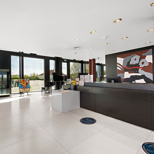 Saguão de hotel moderno com grandes janelas, balcão de recepção, obras de arte e um piano de cauda.