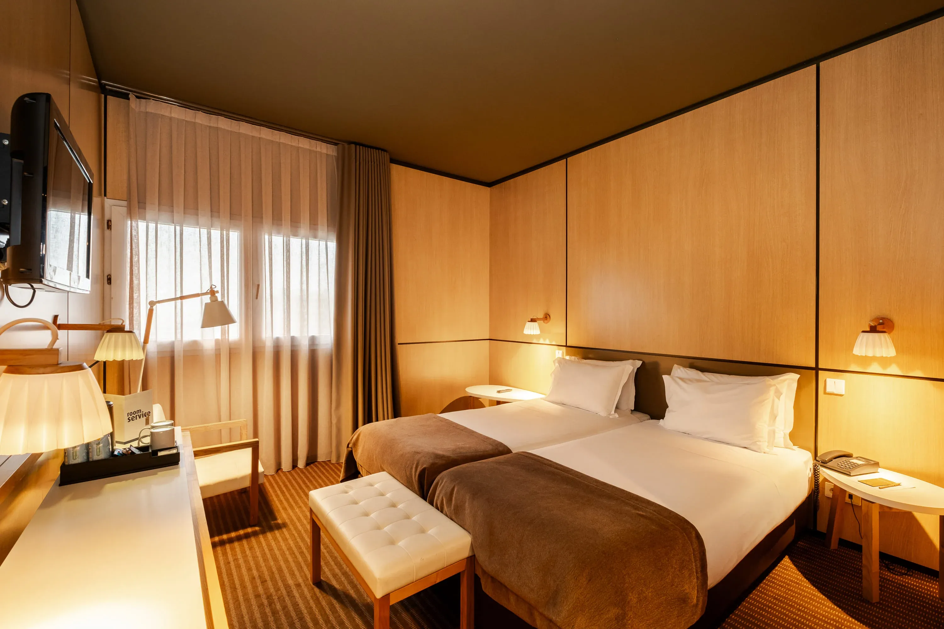 Quarto de hotel moderno com duas camas, mesas de cabeceira, TV e decoração em madeira. Vermar | Axis Hotéis & Golfe | Website Oficial.