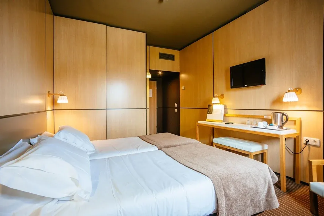 Cama confortável em quarto de hotel moderno com TV e mesa de trabalho. Vermar | Axis Hotéis & Golfe | Website Oficial