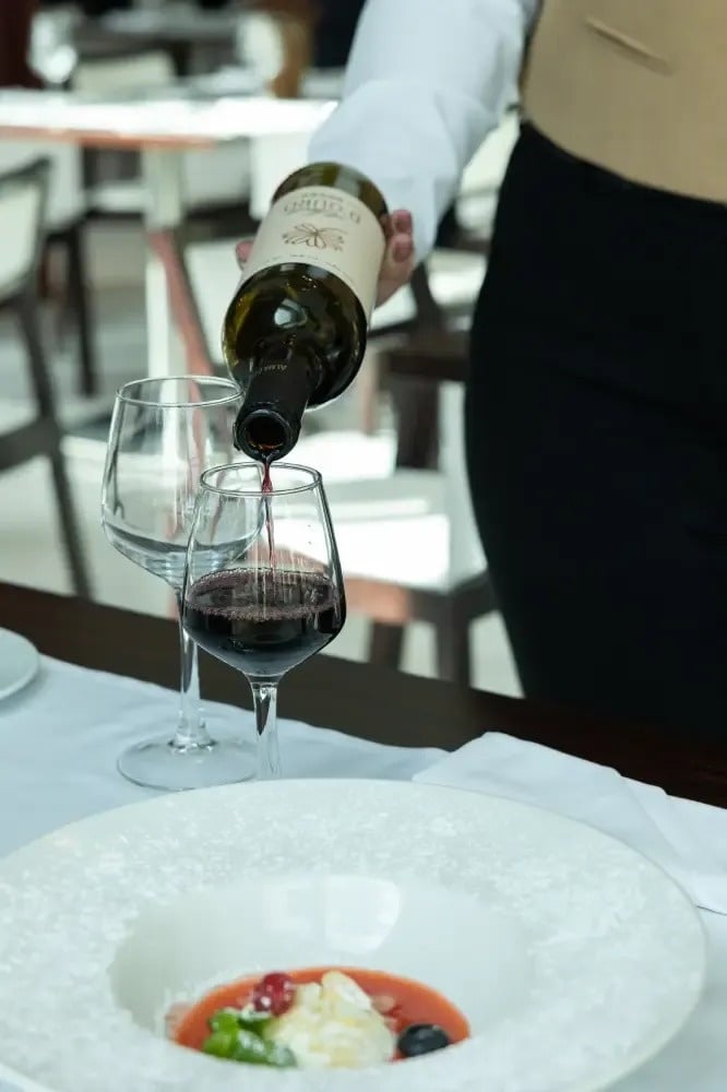 un serveur verse du vin dans un verre à côté d' une assiette de nourriture