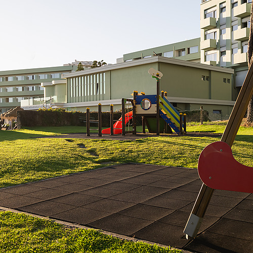 Parque infantil de hotel con columpios y tobogán, ideal para familias Axis: Corporate.