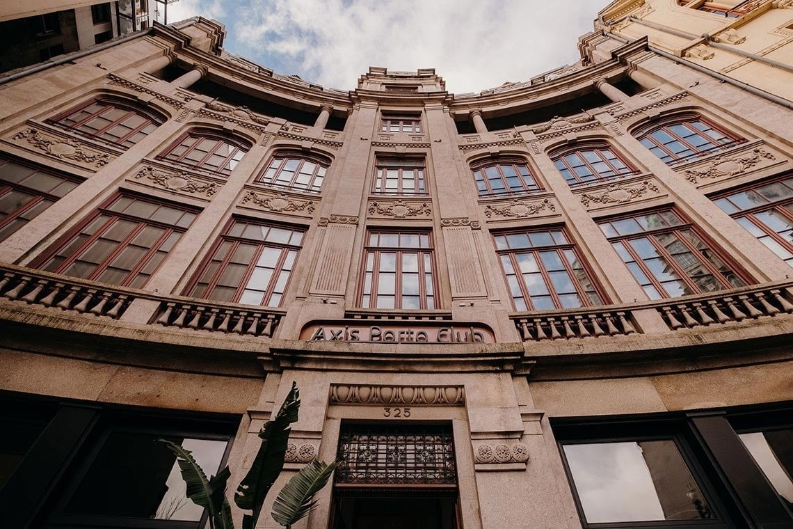 Uma vista de baixo para cima revela a fachada curva e detalhada de um edifício antigo com múltiplas janelas de caixilhos avermelhados, adornado com a placa 
