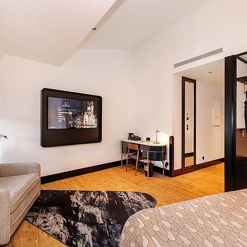 Quarto de hotel moderno com TV, escrivaninha e poltrona. Veja mais em nosso Axis: Corporate.
