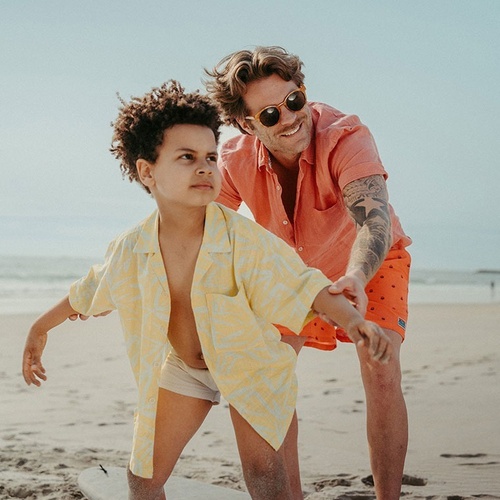 a man and a boy are standing on a surfboard on the beach