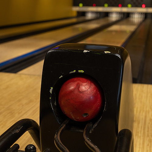Bola de boliche roja en dispensador, lista para jugar en las pistas de nuestro hotel. Axis: Corporate