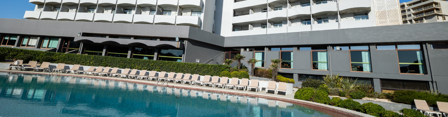 Piscina e espreguiçadeiras com hotel ao fundo. Vermar | Axis Hotéis & Golfe | Website Oficial.