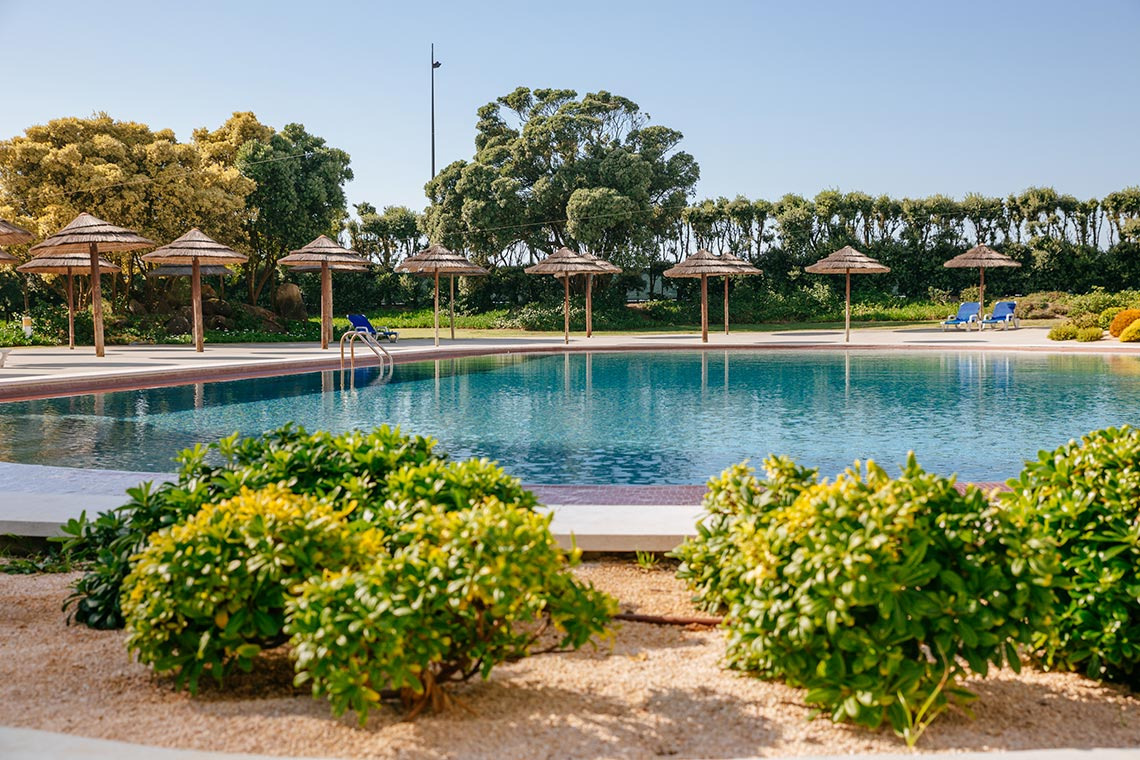 Piscina de luxo com espreguiçadeiras e guarda-sóis de palha, ideal para o seu Vermar | Axis Hotéis & Golfe | Website Oficial.