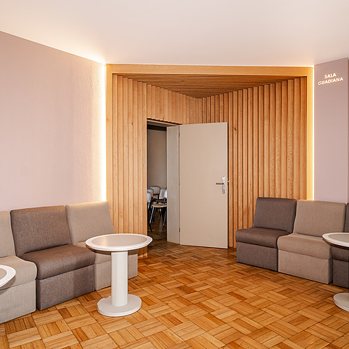Sofás y mesas en la sala de espera del hotel, con decoración en madera y luz cálida. Axis: Corporate