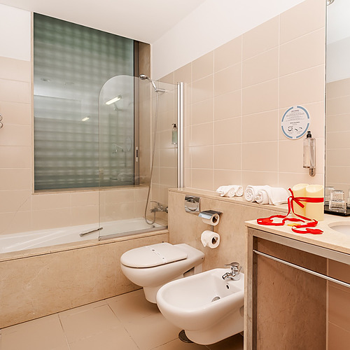 Elegante baño de hotel con bañera, inodoro, bidé y lavabo. Axis: Corporate con amenidades.
