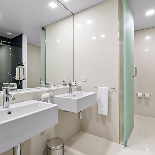 Um banheiro moderno e minimalista com duas pias brancas, um grande espelho e um chuveiro de vidro fosco.