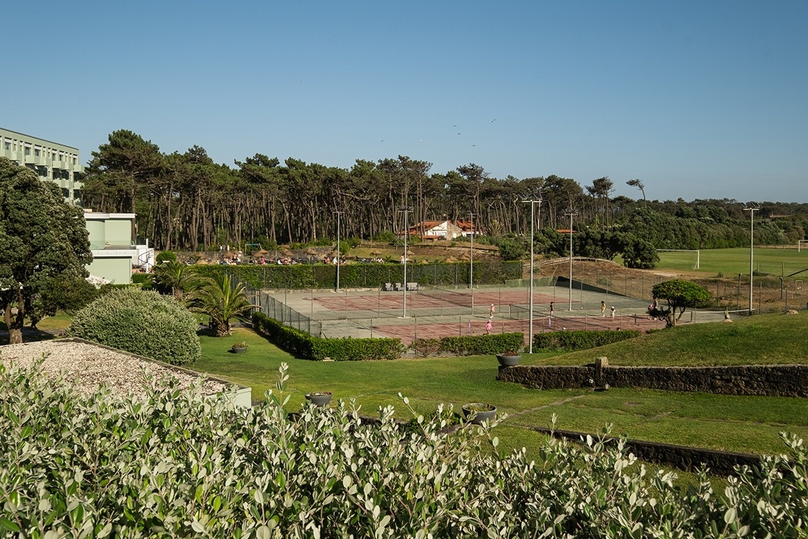 um campo de tênis cercado por árvores com um prédio ao fundo