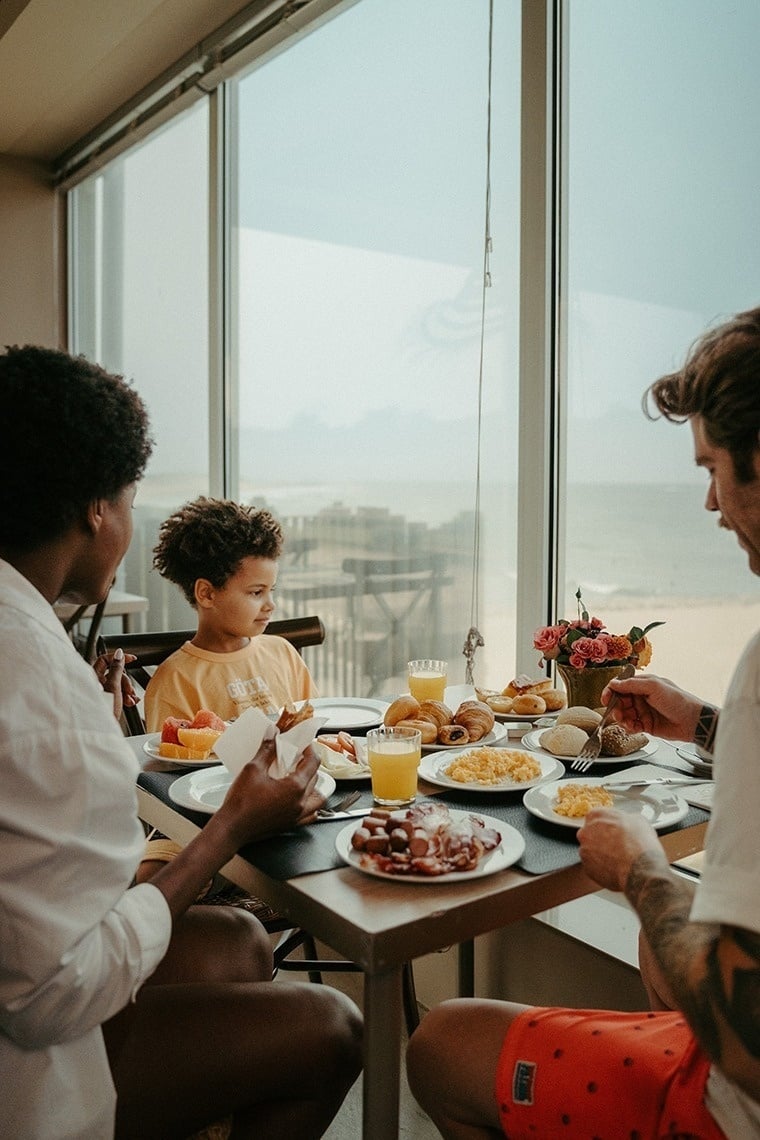 uma família está sentada em uma mesa comendo comida e bebendo suco de laranja