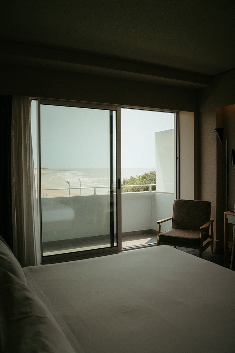 um quarto com uma cama e uma cadeira e uma porta de vidro com vista para o oceano