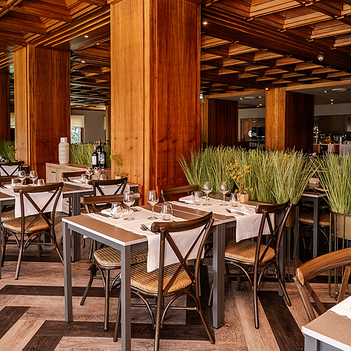Sala de jantar com mesas postas, cadeiras de vime e teto de madeira. Axis: Corporate