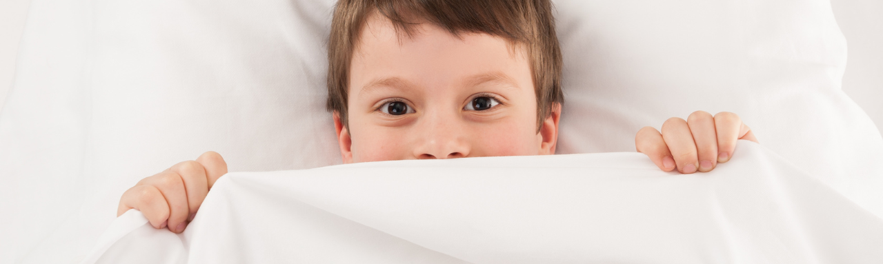 a young boy peeking out from under a white blanket