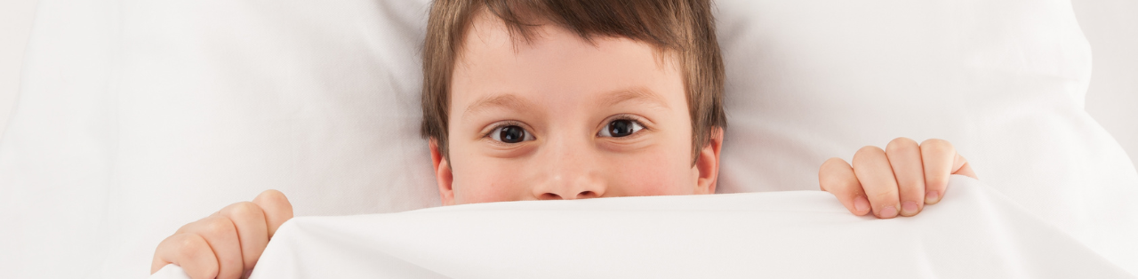 a young boy is hiding under a blanket in bed .