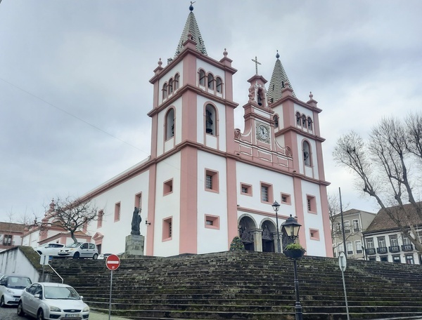 una iglesia rosa y blanca con coches estacionados frente a ella