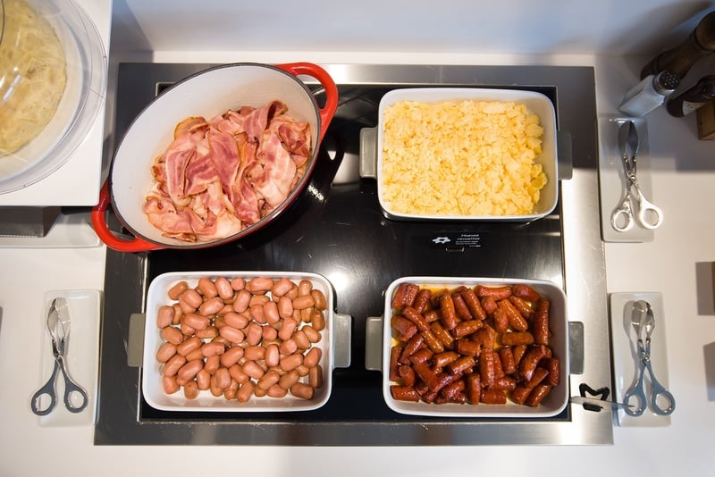 une cuisinière avec un pot de bacon , des œufs brouillés , des haricots et des hot-dogs