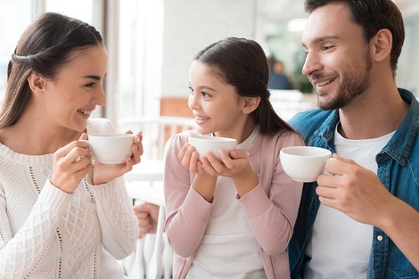un hombre , una mujer y una niña sostienen tazas de café en sus manos