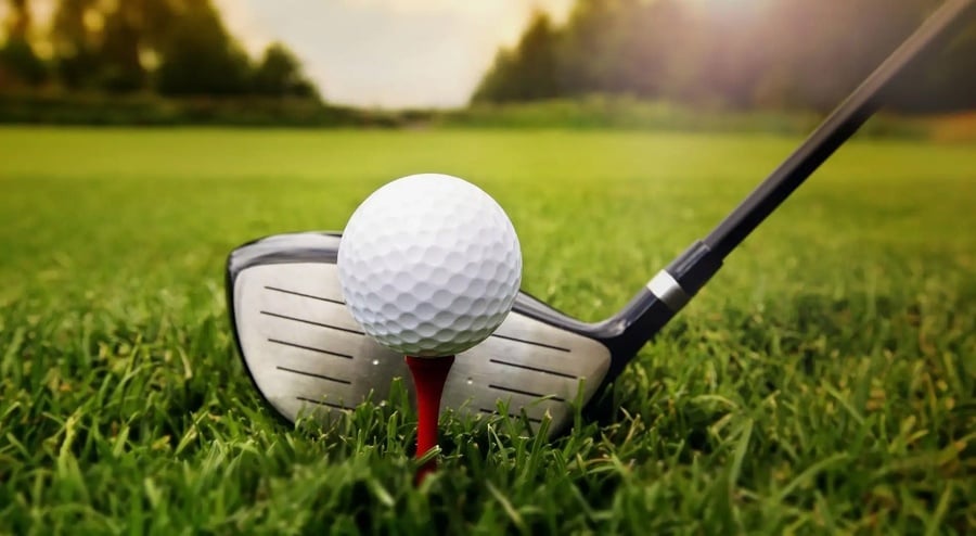Bola de golfe no tee em frente ao driver no gramado de um campo de golfe.