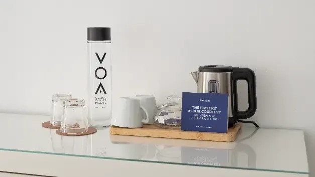 uma mesa com uma garrafa de água , uma chaleira , copos e um cartão .