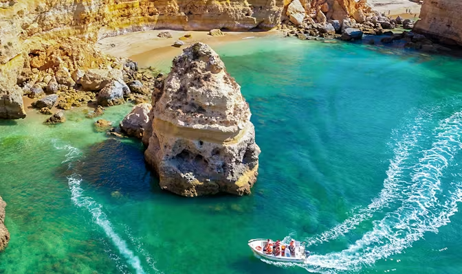 Um barco navega em águas azul-turquesa cristalinas de uma enseada rochosa com uma praia de areia.