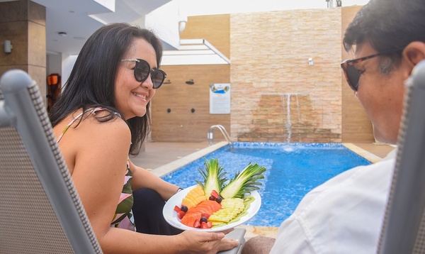 una mujer sostiene un plato de frutas frente a una piscina