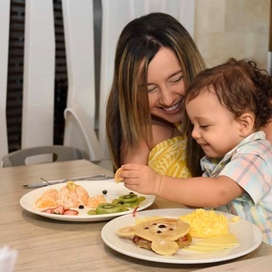 una mujer y un niño están sentados en una mesa comiendo panqueques y frutas