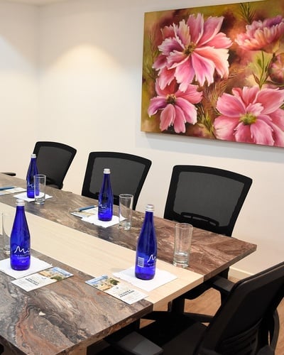 una mesa de conferencias con botellas y vasos y un cuadro de flores en la pared