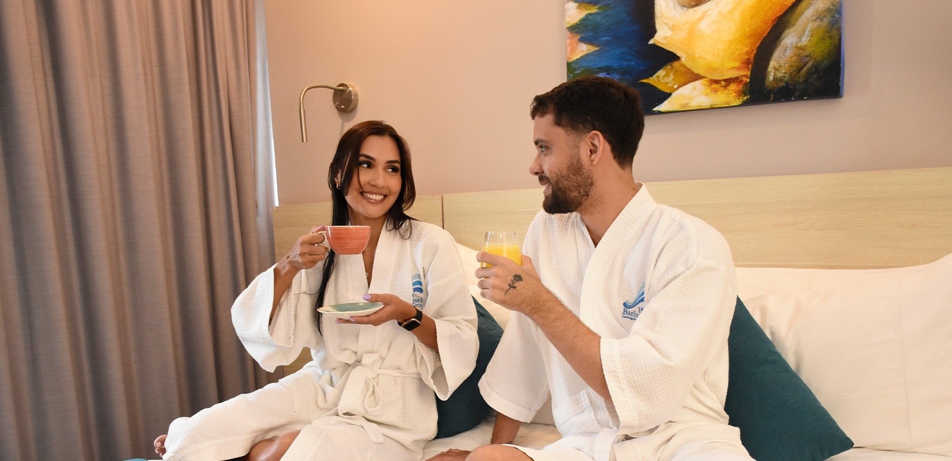 a man and a woman are sitting on a bed drinking orange juice