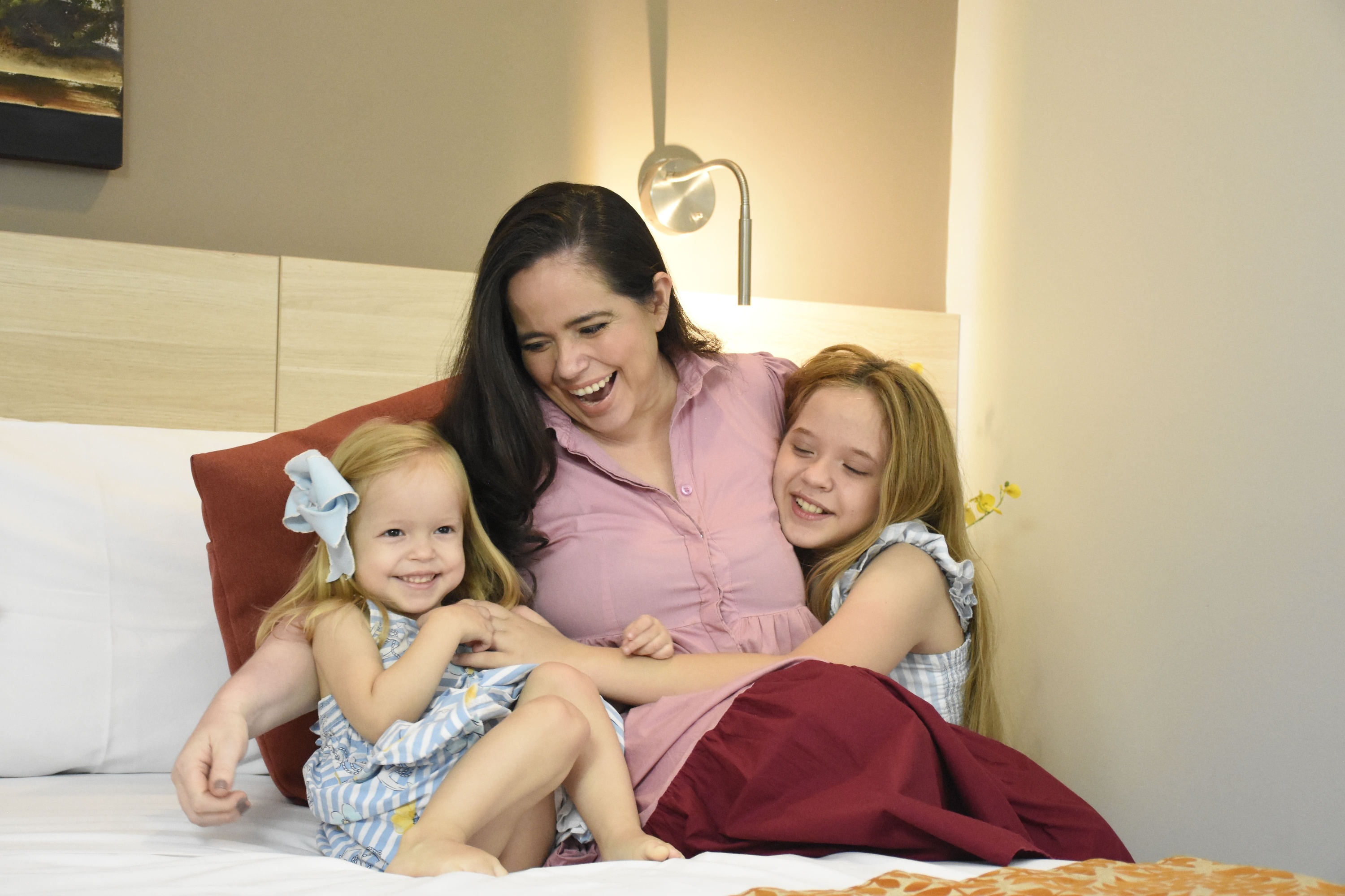 a woman sits on a bed with two little girls