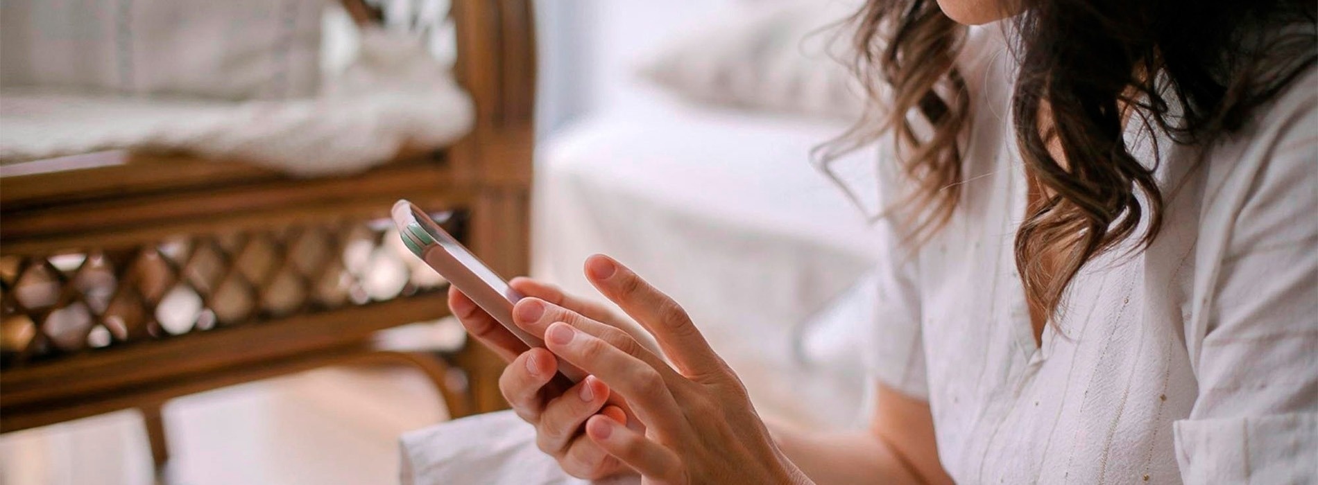 una mujer con un vestido blanco está sentada en un sofá usando un teléfono inteligente