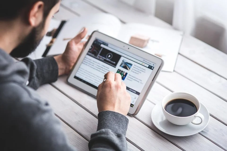 a man sits at a table using a tablet and a cup of coffee
