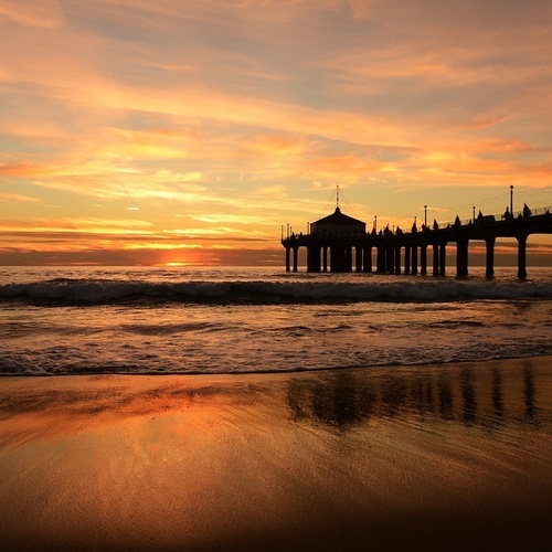 una playa al atardecer con un muelle en el fondo