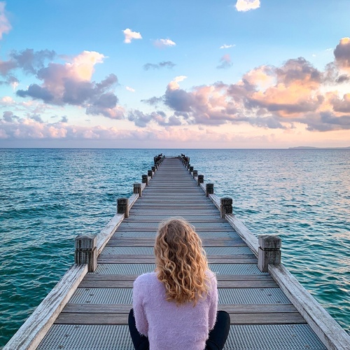 una mujer sentada en un muelle mirando al océano